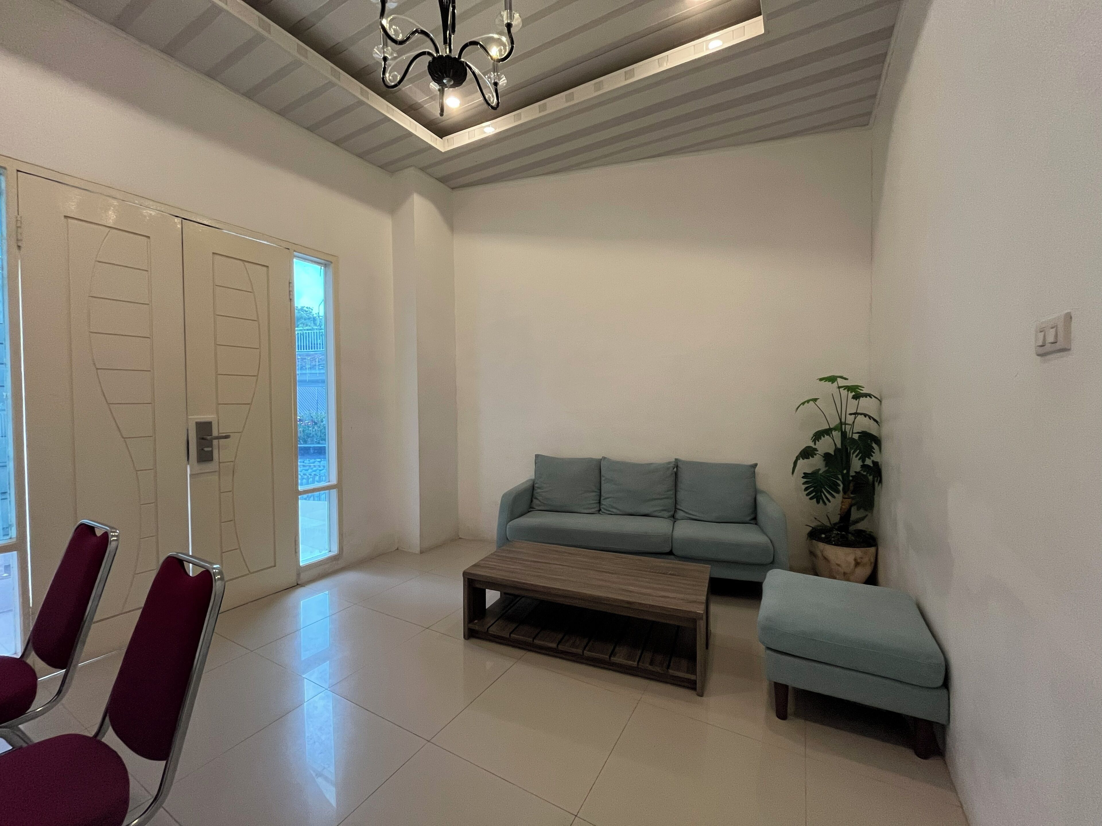 Un'ampia zona living con un divano blu chiaro, un tavolino in legno e un poggiapiedi. Si notano due poltrone rosse e una pianta in vaso.