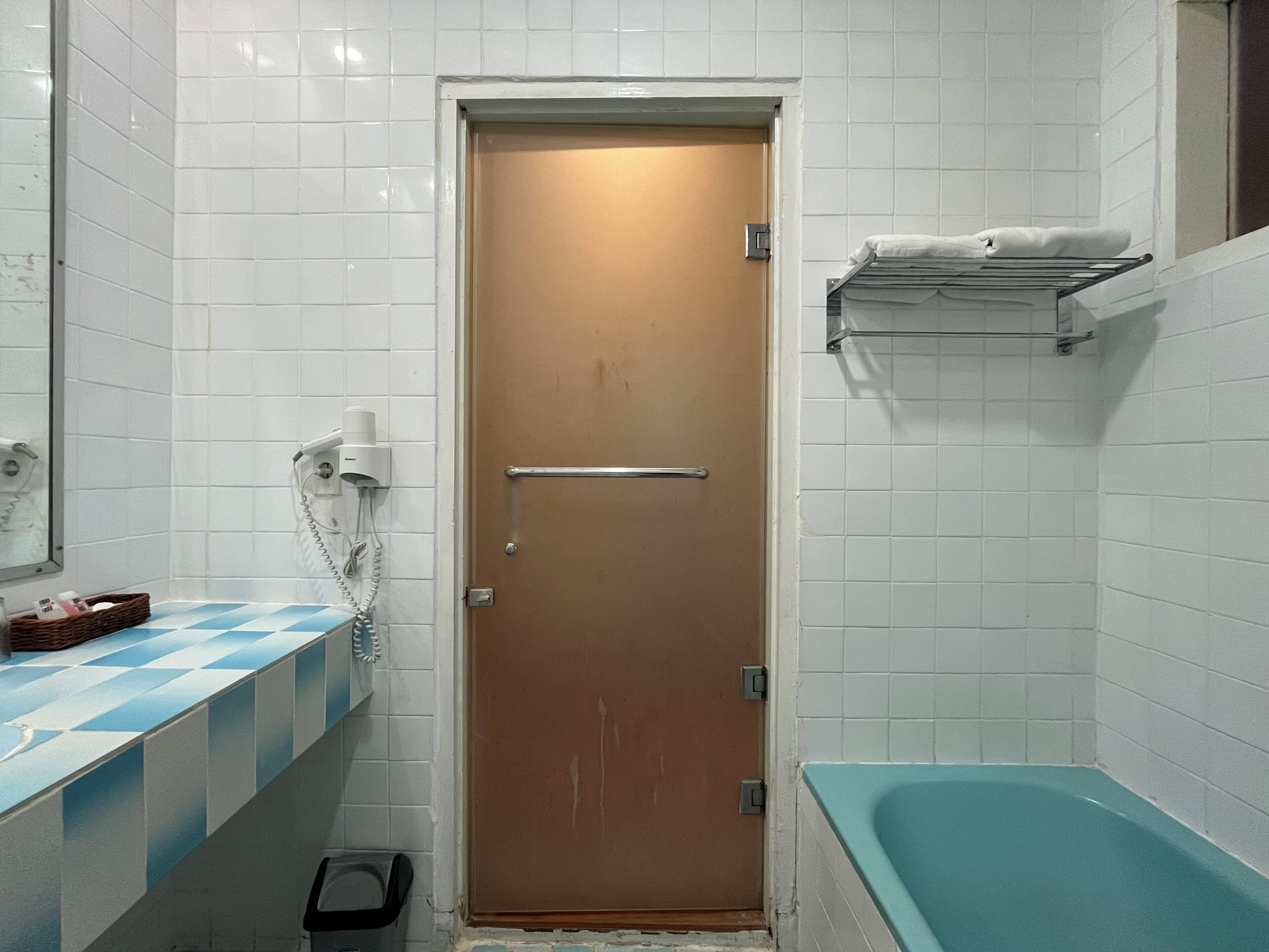 Ein Badezimmer mit einer braunen Tür, einer blau karierten Arbeitsplatte, einer weißen Fliesenwand, einer weißen Badewanne und einem Handtuchhalter mit Handtüchern.