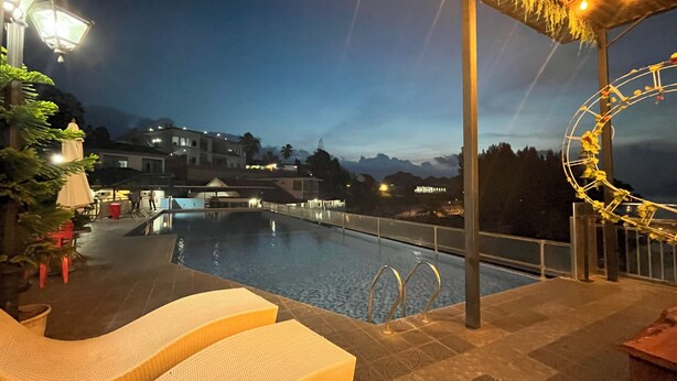 Zona junto a la piscina con sillones reclinables, piscina y vista a edificios al fondo.