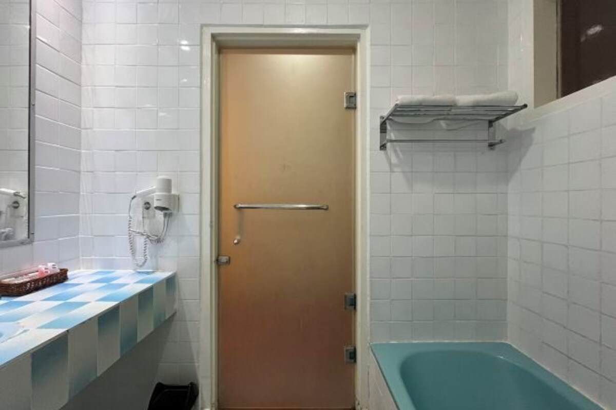 A bathroom with white tiled walls, a wooden door, a blue checkered countertop, a sink, a mirror, a towel rack, and a bathtub.