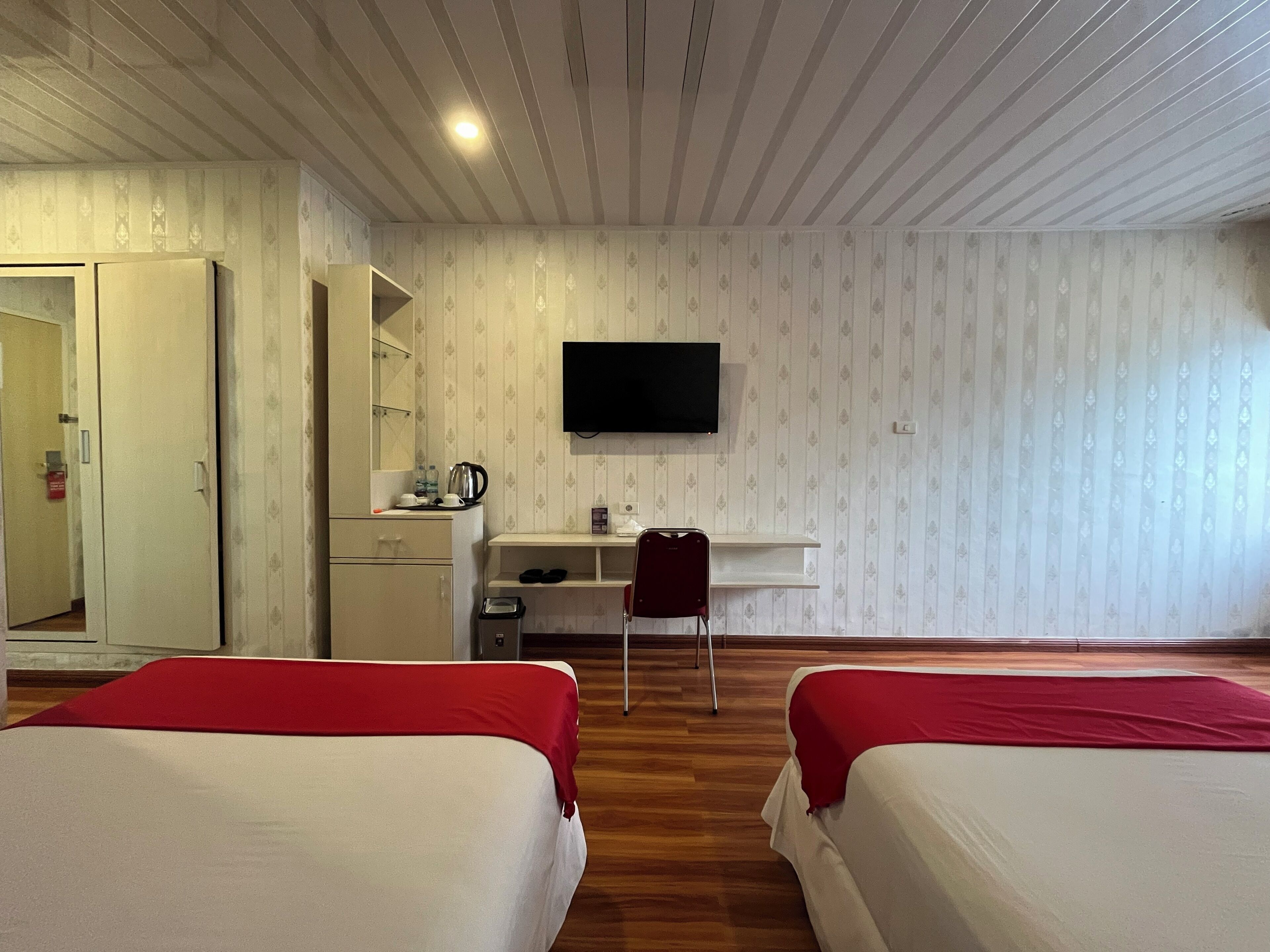 A hotel room with two beds, a desk with a chair, a television, and a wardrobe.