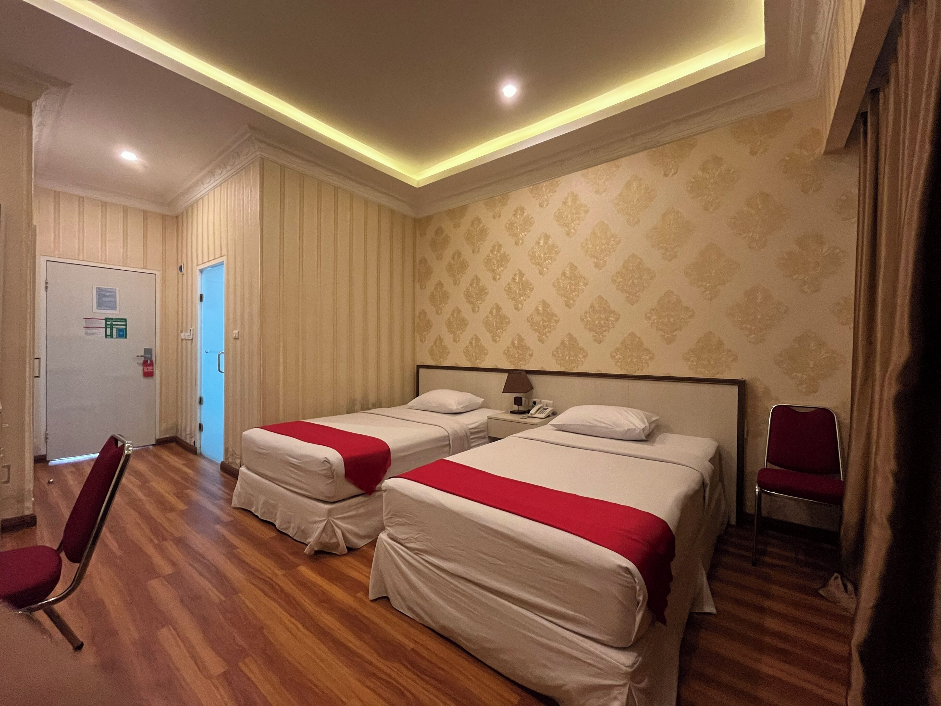 Une chambre d’hôtel avec deux lits, un plancher en bois, un mur à motifs et une porte signalant les issues de secours.