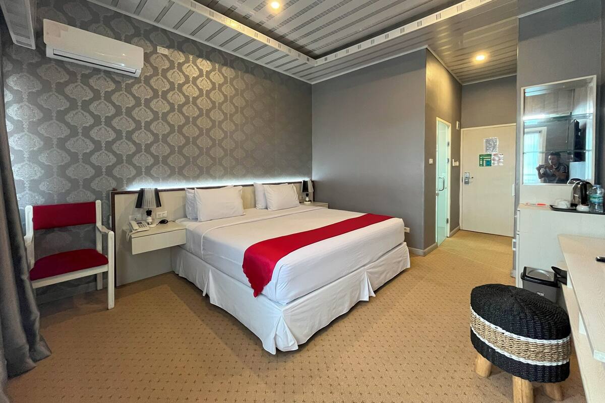 Una habitación de hotel con una cama grande, un escritorio, una silla, un espejo y un taburete pequeño.