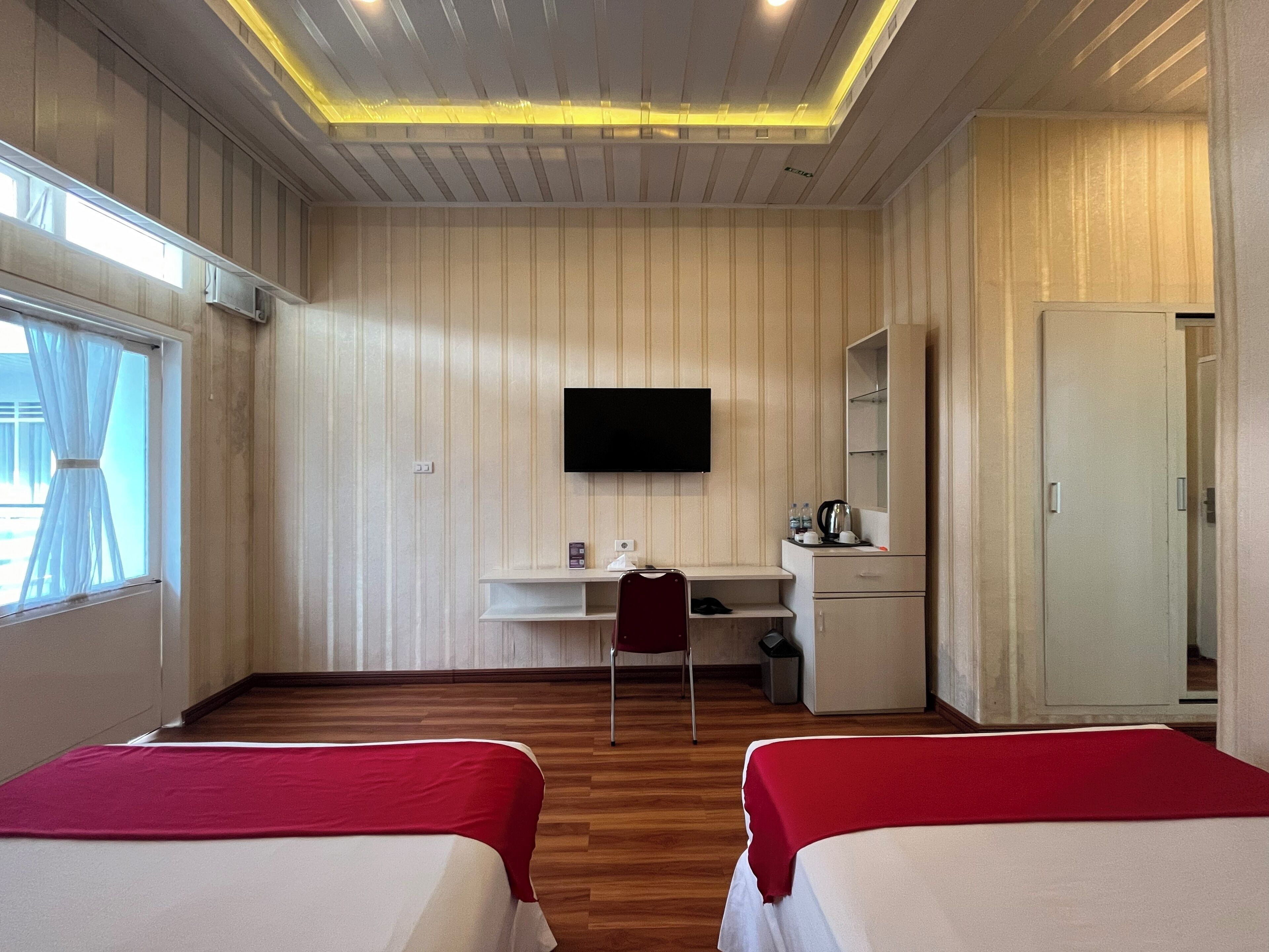 A hotel room with two beds, a desk, a TV, a wardrobe, and a window with curtains.