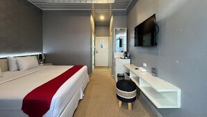 Una habitación de hotel con una cama, un escritorio, un televisor y un taburete pequeño.