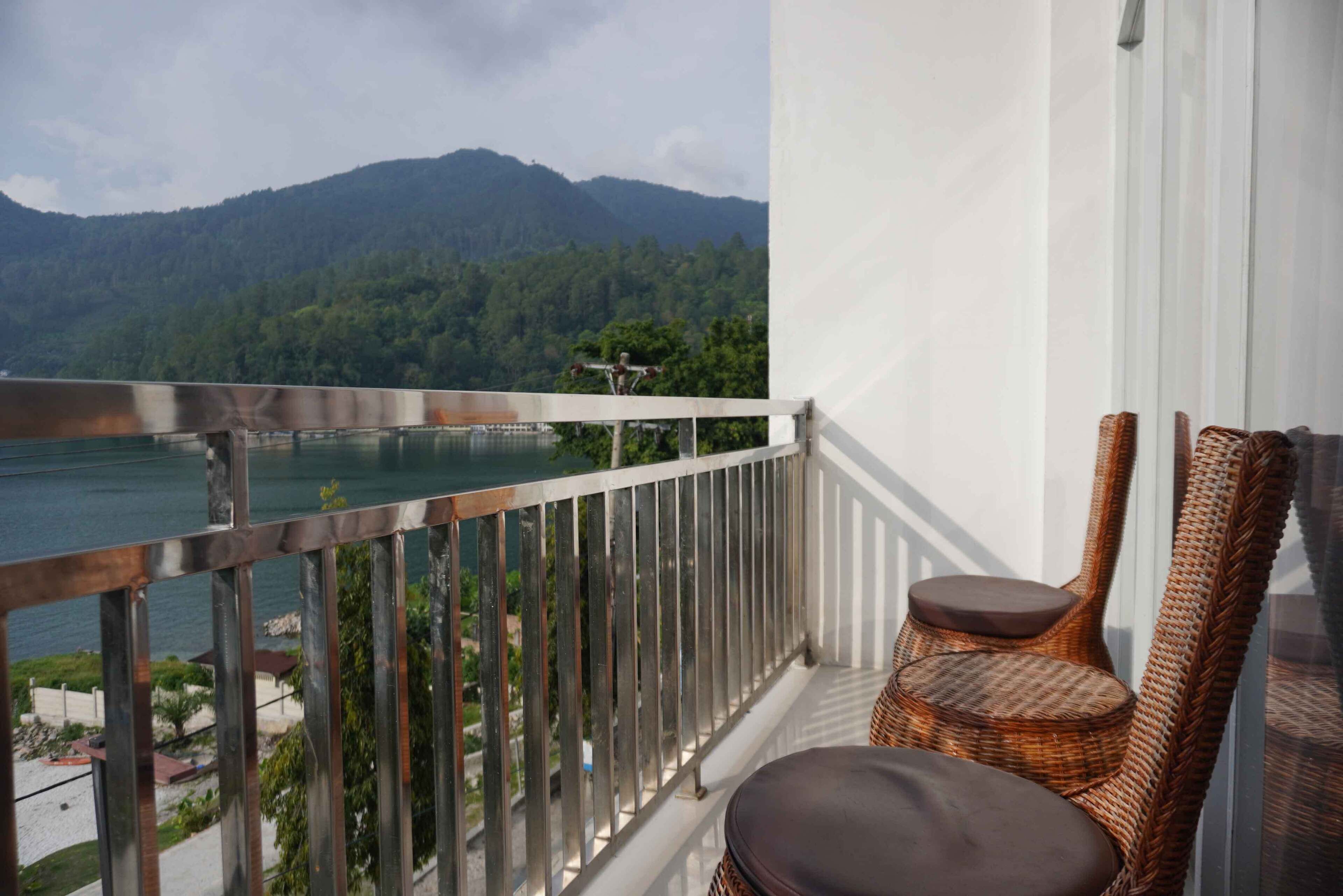A balcony with a view of a lake and mountains, wicker chairs, and a small table.