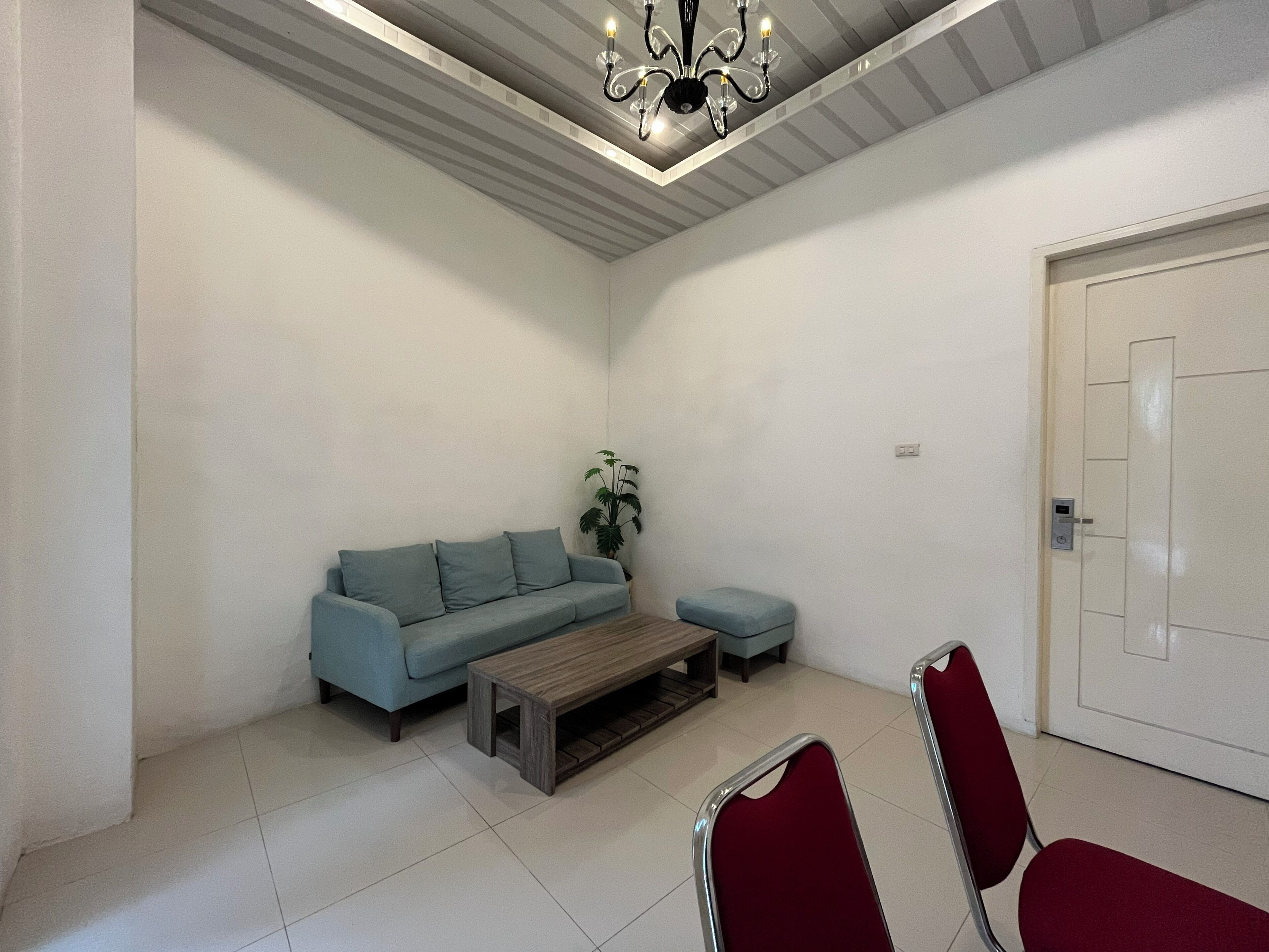 A room with a sofa, a small table, two chairs, a potted plant, and a door.