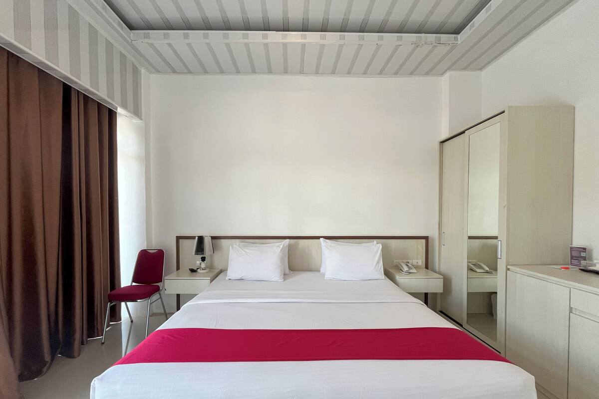 Una habitación de hotel con una cama grande, una mesita de noche con lámpara, teléfono y espejo.