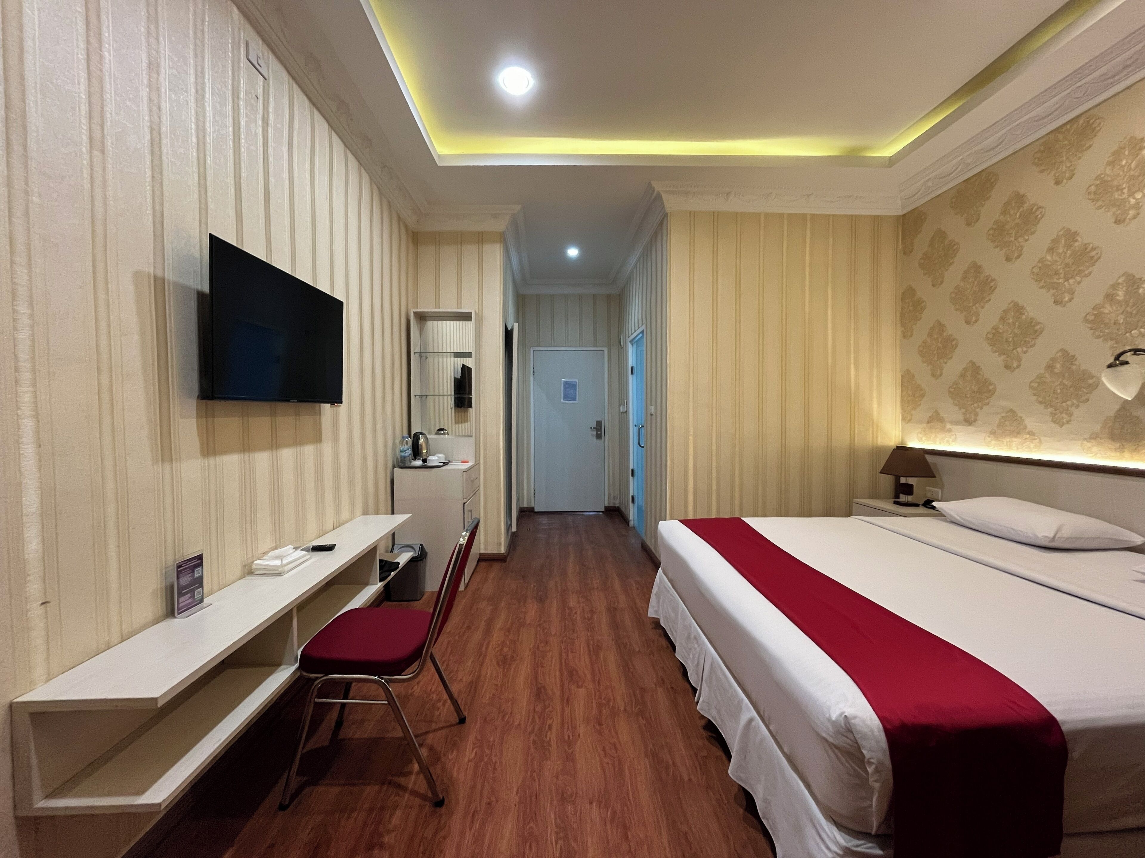 Een hotelkamer met een bed, een bureau met stoel, een televisie, een bedlamp en een deur die leidt naar een andere kamer.