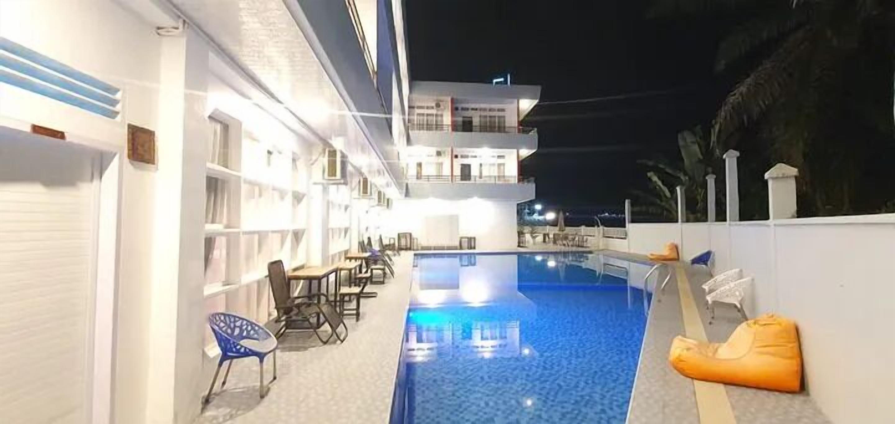 Piscina interna com espreguiçadeiras e mesas, rodeada por um edifício branco com vários andares e varandas.