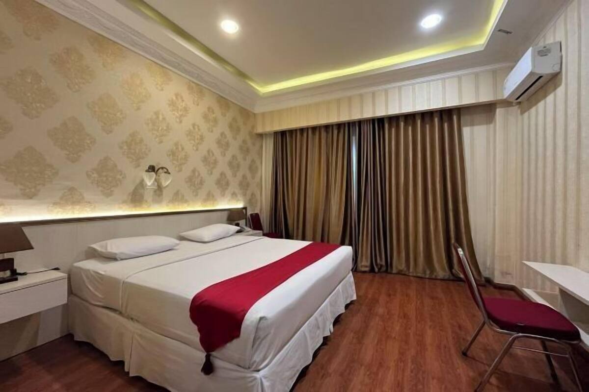 Habitación de hotel con cama, mesita de noche, lámpara, silla y cortinas.