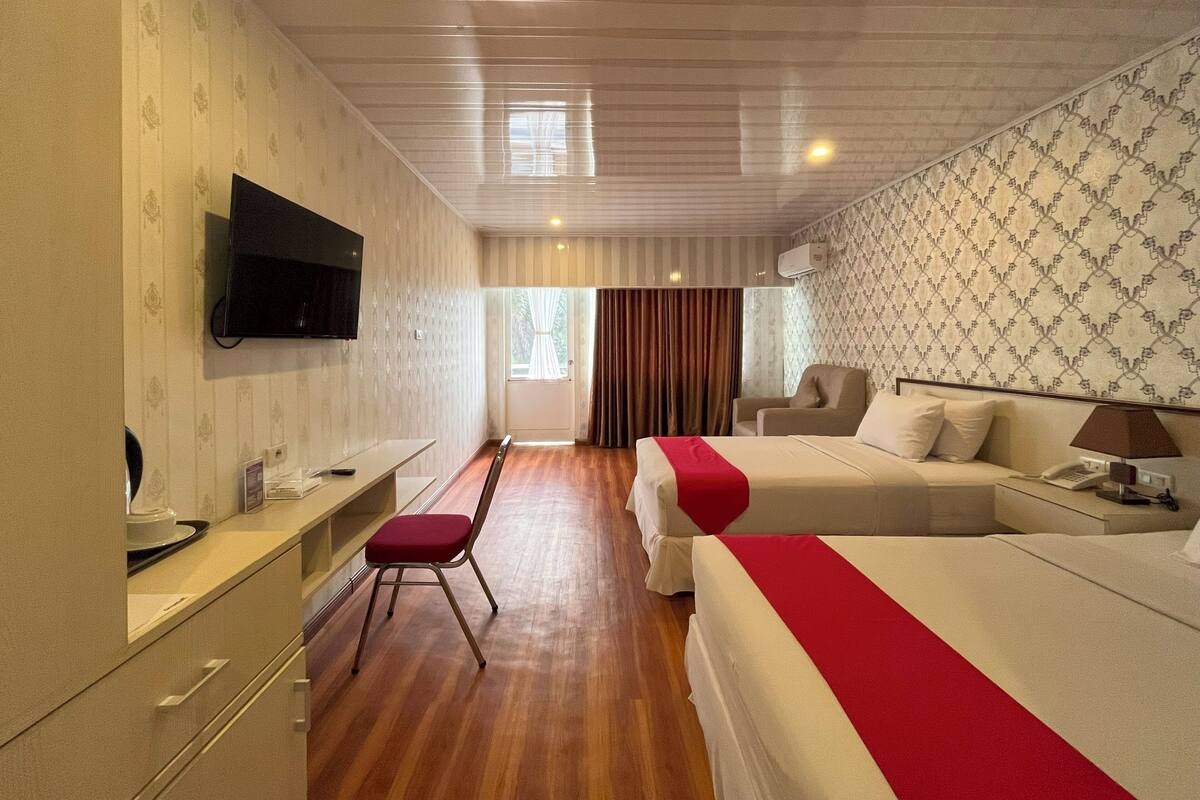 Una habitación de hotel con cama, escritorio, silla, televisión y ventana con cortinas.