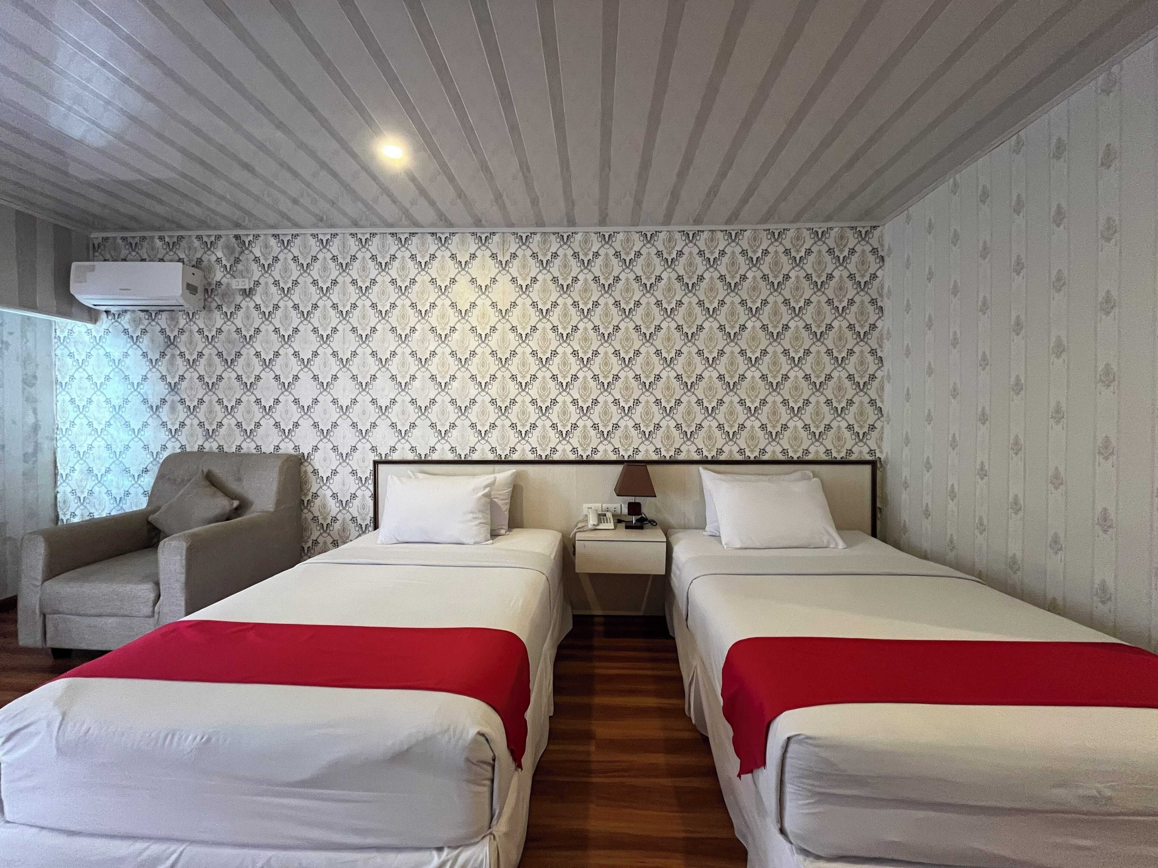 A hotel room with two beds, a chair, a nightstand, and patterned wallpaper.