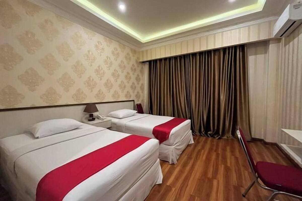 Habitación de hotel con dos camas, un escritorio, una silla y un aire acondicionado.