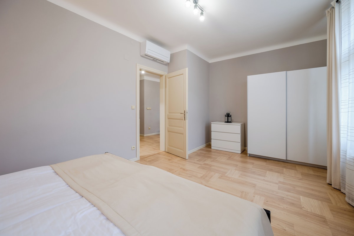 A bedroom with a bed, a wardrobe, a bedside table, and an air conditioning unit.