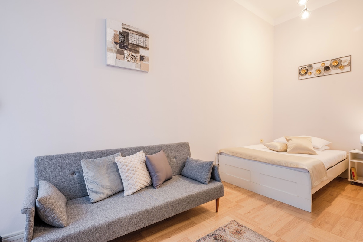 A modern bedroom with a grey sofa, a white bed, and a small bedside table.