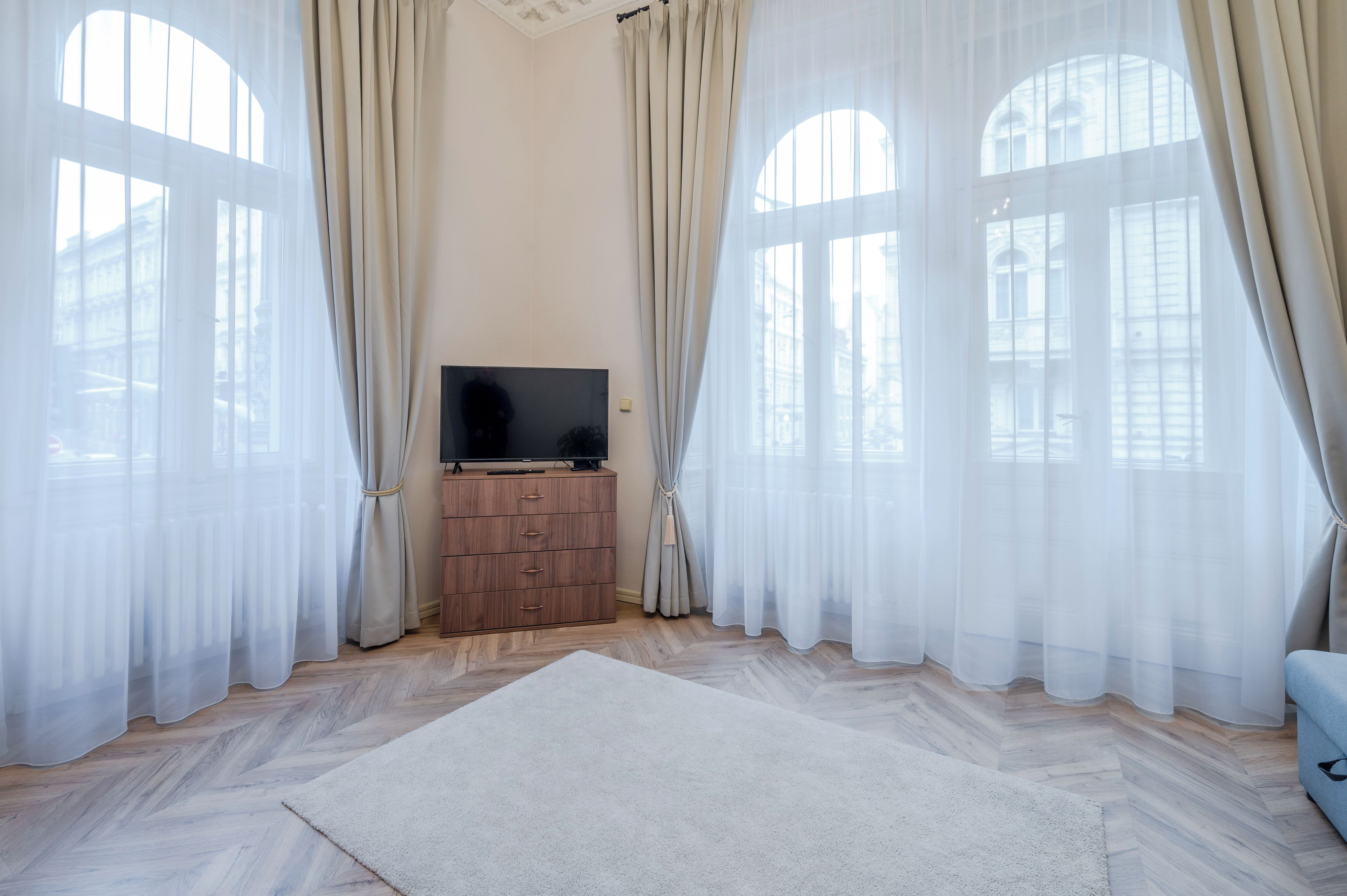 Una stanza con ampie finestre, una televisione a schermo piatto su un mobile in legno e un tappeto bianco sul pavimento.
