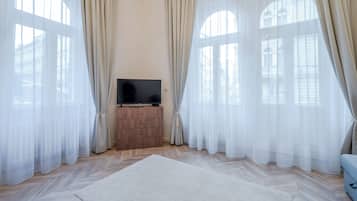 Una stanza con ampie finestre, una televisione a schermo piatto su un mobile in legno e un tappeto bianco sul pavimento.