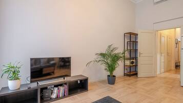 Una sala de estar moderna con una televisión de pantalla plana, una estantería, una planta en maceta y una puerta que da a otra habitación.
