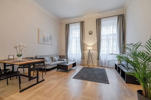 A modern living room with a sofa, a dining table, and a coffee table. There is a large window with curtains, a floor lamp, and a potted plant. - Palace Petrarca Apartments (Prague)