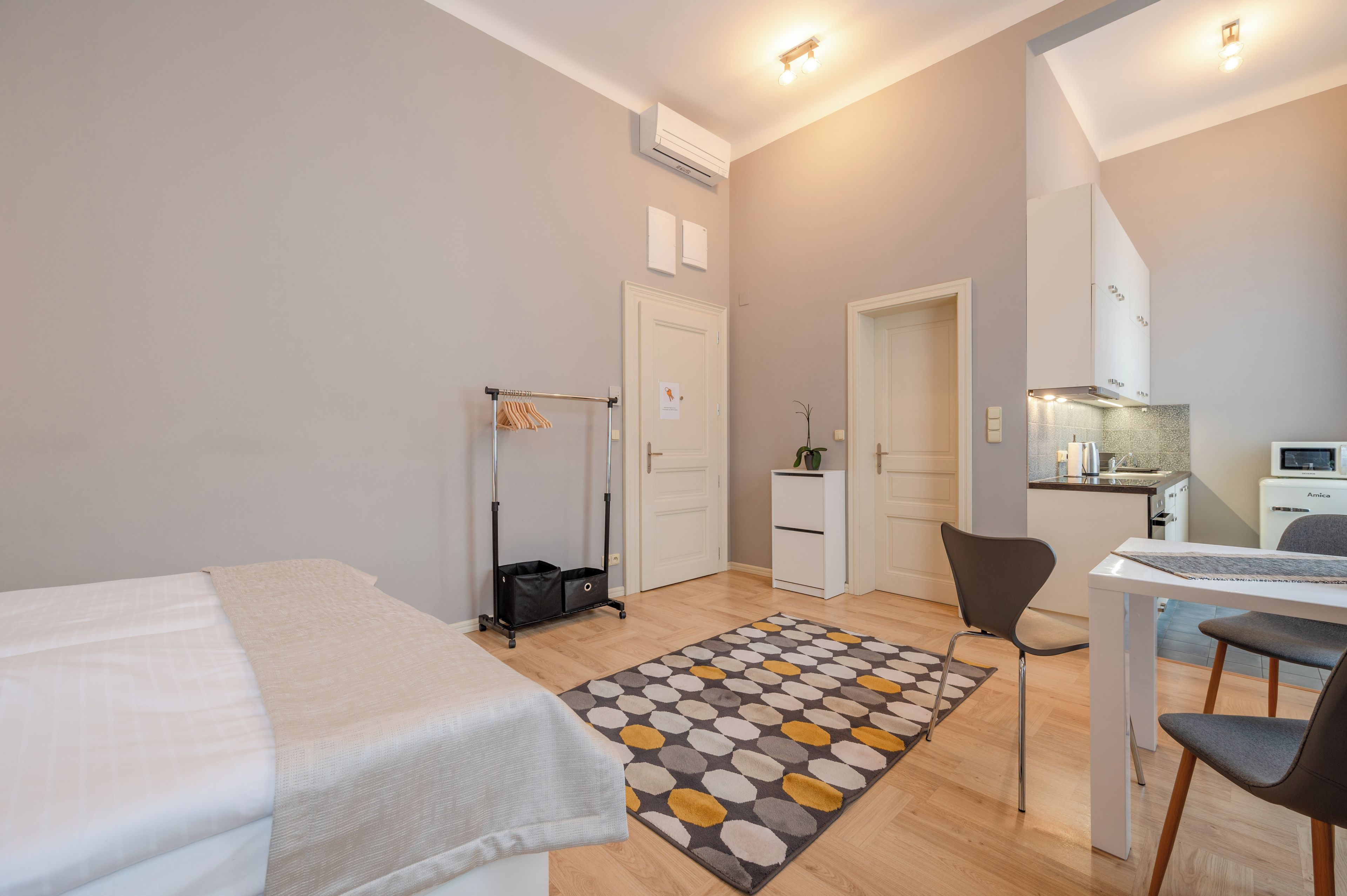 Une chambre d’hôtel moderne équipée d’un lit, d’un bureau, d’une chaise, d’une petite kitchenette et d’une salle de bain.