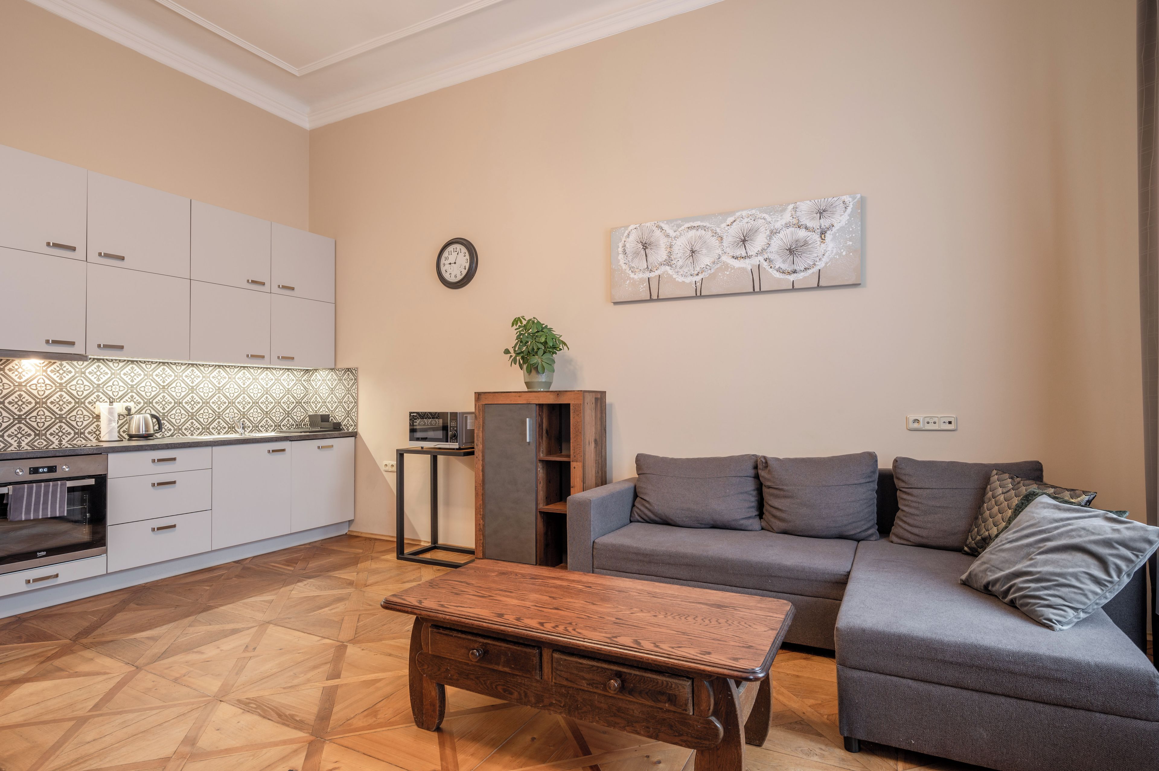 Un espace de vie moderne comprenant un coin cuisine, un ensemble de canapés, une table basse et une horloge murale.