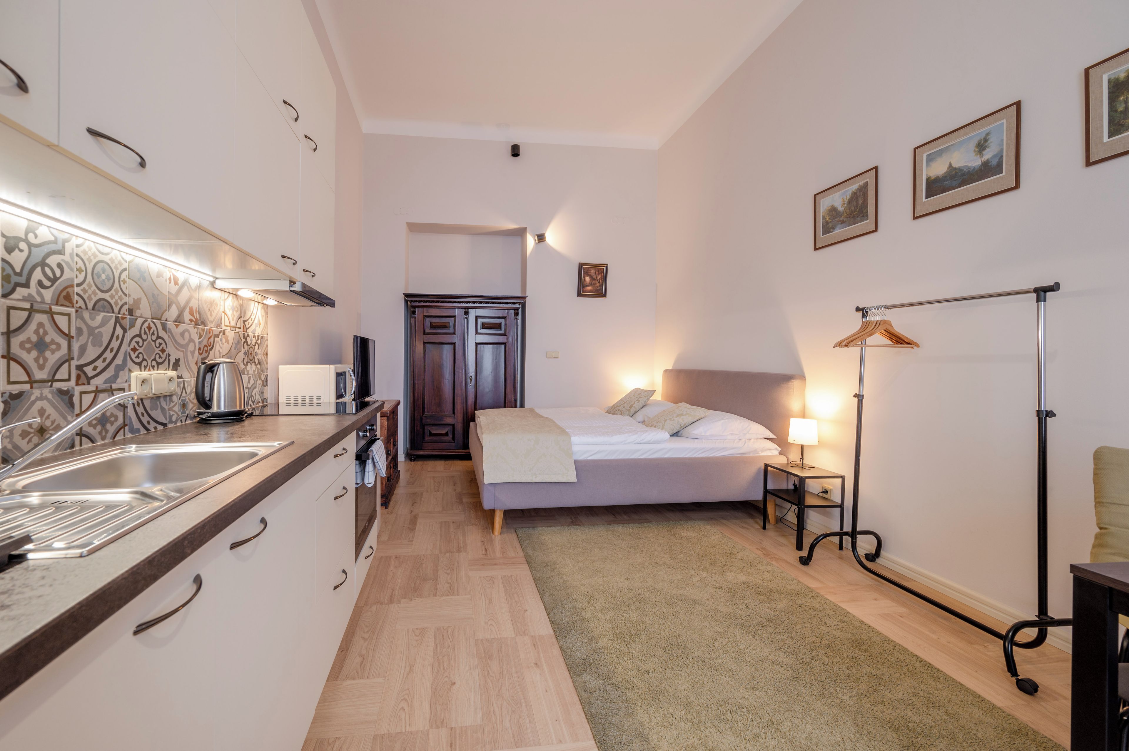 Une chambre d’hôtel compacte comprenant un coin cuisine, un lit avec une table de chevet, une lampe sur pied et une petite table de chevet avec une lampe.