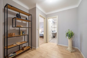 A hallway with a wooden bookshelf, a potted plant, and a glimpse of a bedroom with a bed and a bathroom. - Palace Petrarca Apartments (Prague)