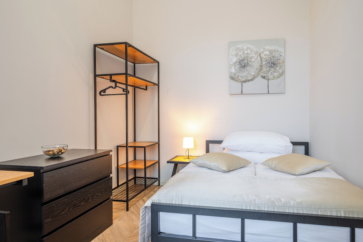 A bedroom with a bed, bedside table, lamp, and a tall wardrobe with shelves.