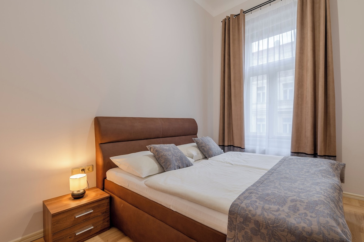 A bedroom with a bed, bedside table, lamp, and curtains.