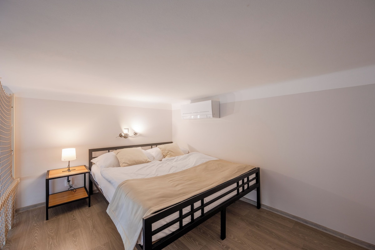 A single bed with a wooden frame, a bedside table with a lamp, and a wall-mounted air conditioner.