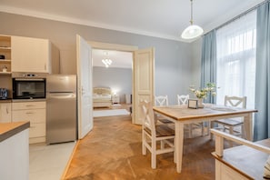 A modern kitchen with a stainless steel refrigerator and oven, a dining area with a wooden table and chairs, and a bedroom with a bed and nightstand. - Palace Petrarca Apartments (Prague)