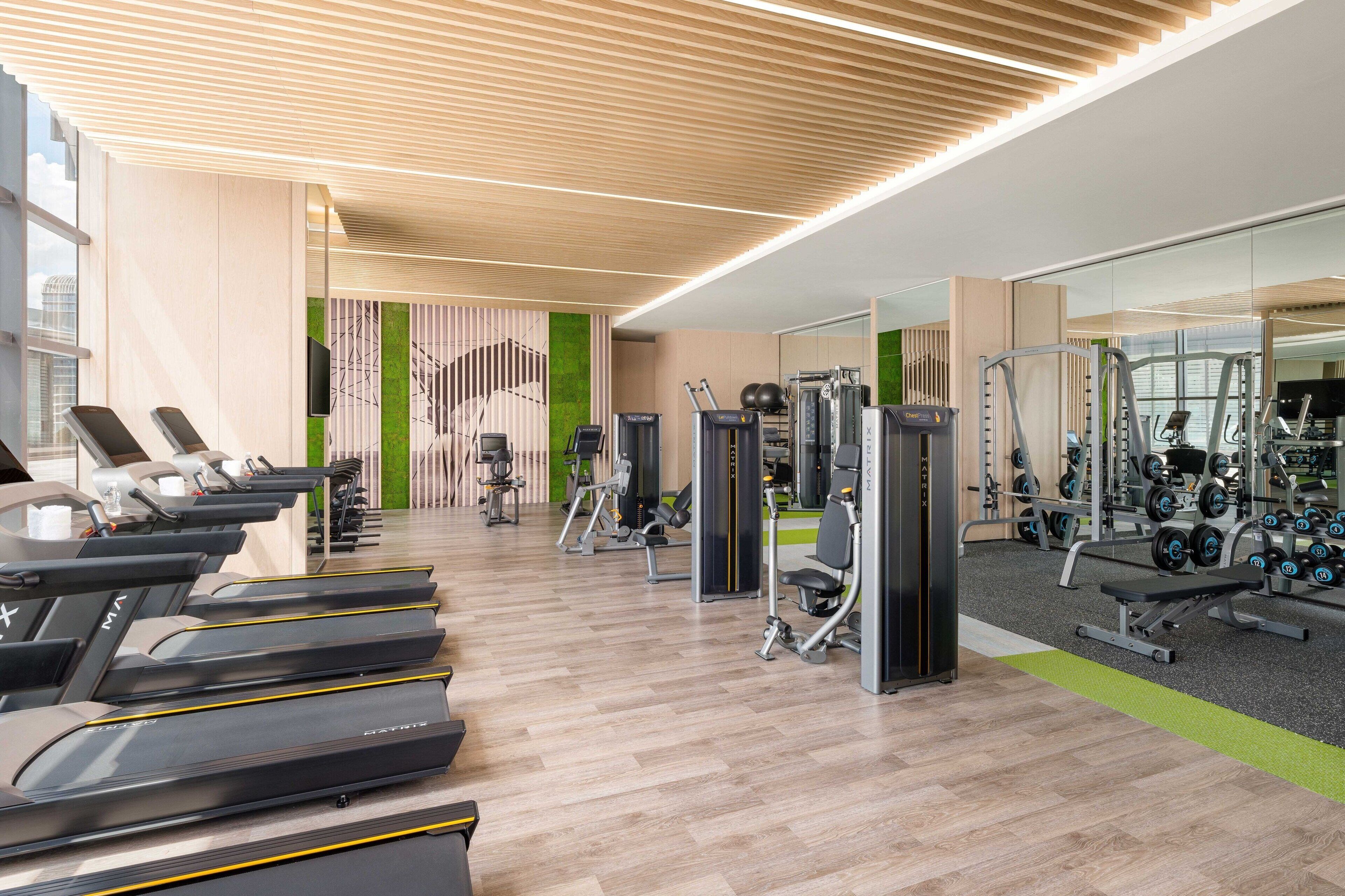 Ett modernt gym med löpband, styrketräningsmaskiner och en grön vägg.