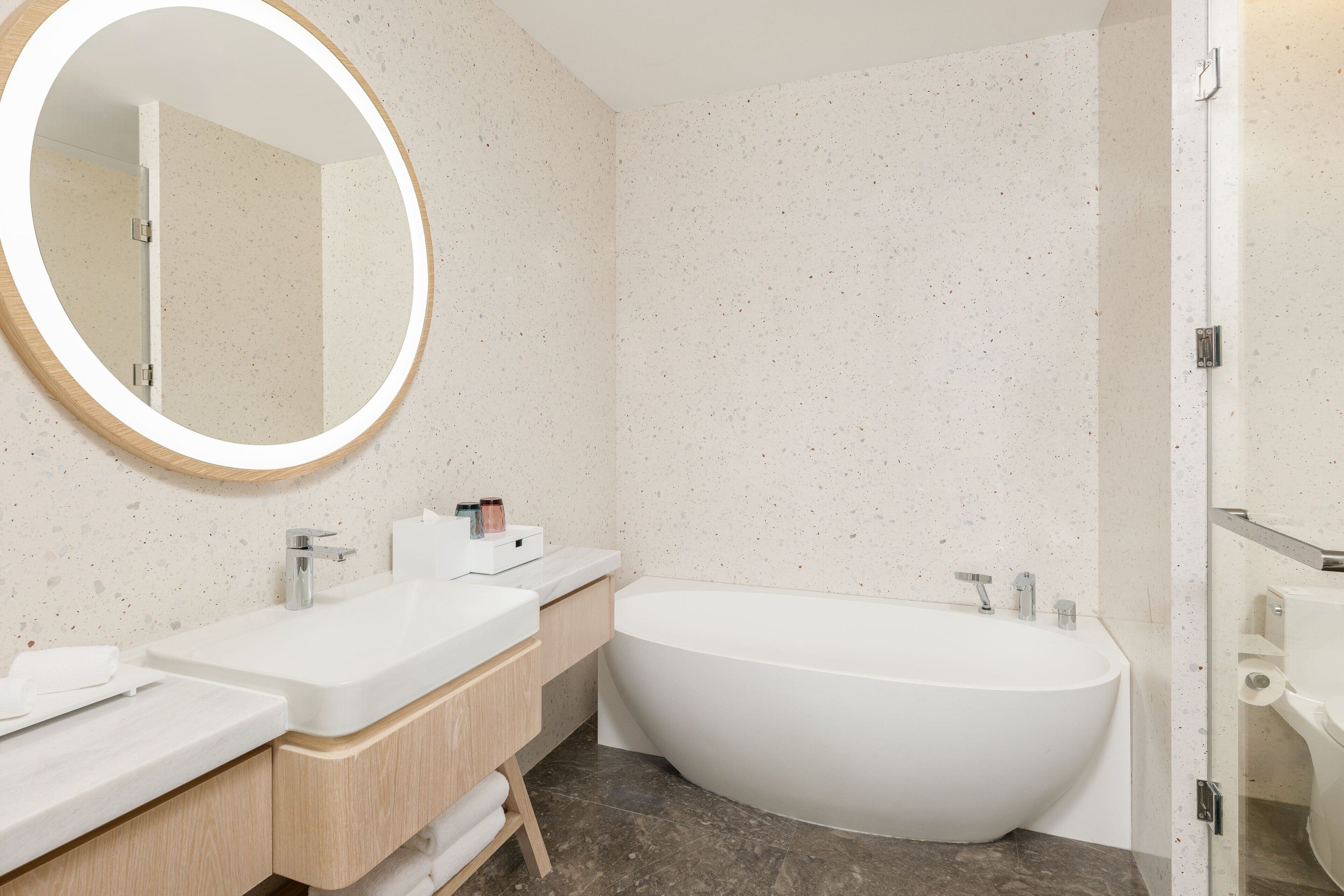 Un baño moderno con una bañera independiente, un espejo redondo y un mueble de tocador doble.