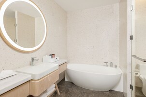 Un baño moderno con una bañera independiente, un espejo redondo y un mueble de tocador doble.