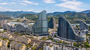 A modern cityscape with distinctive curved skyscrapers, a river, and mountains in the background.