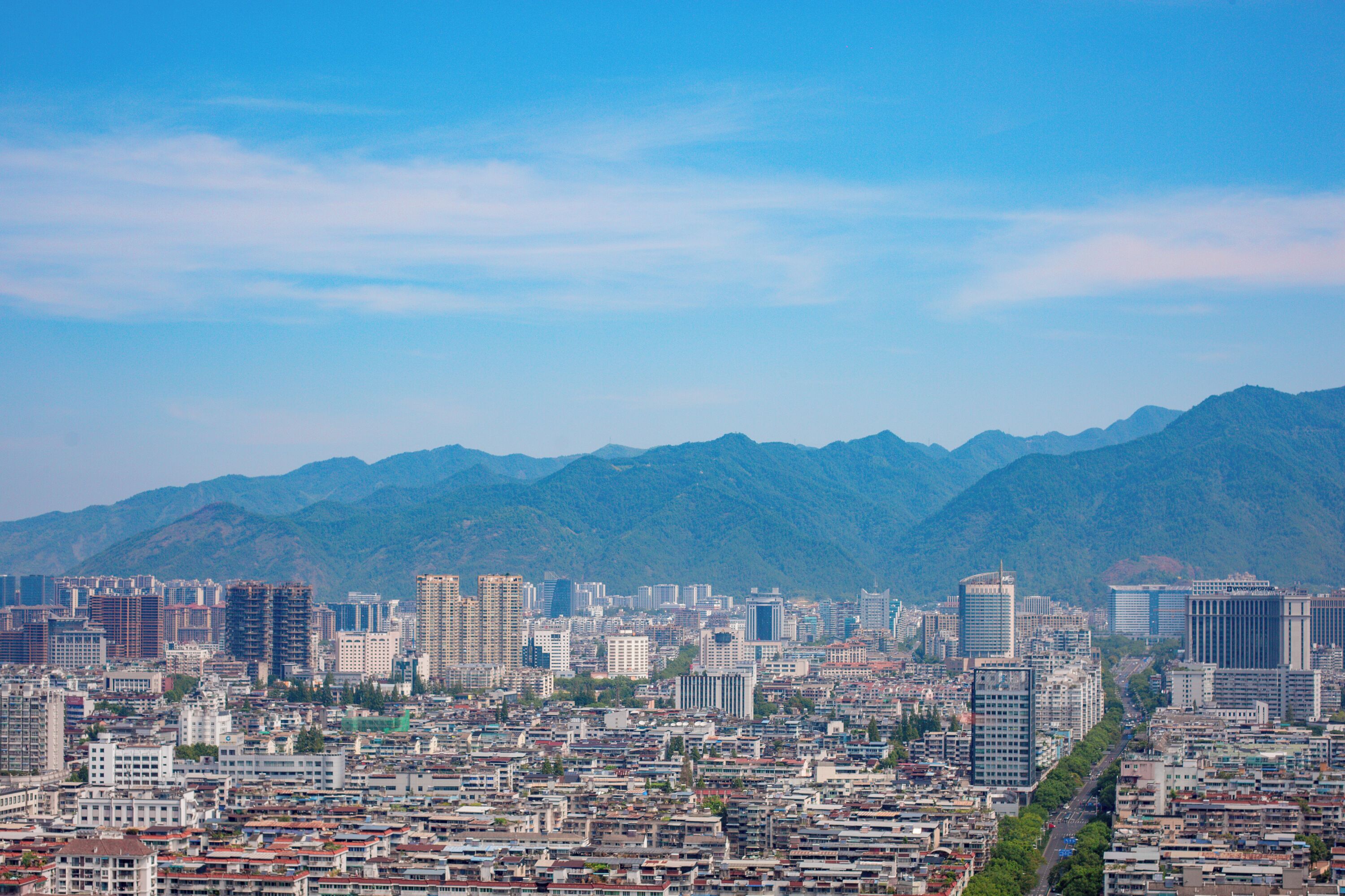 A cityscape with a dense urban area and mountains in the background.