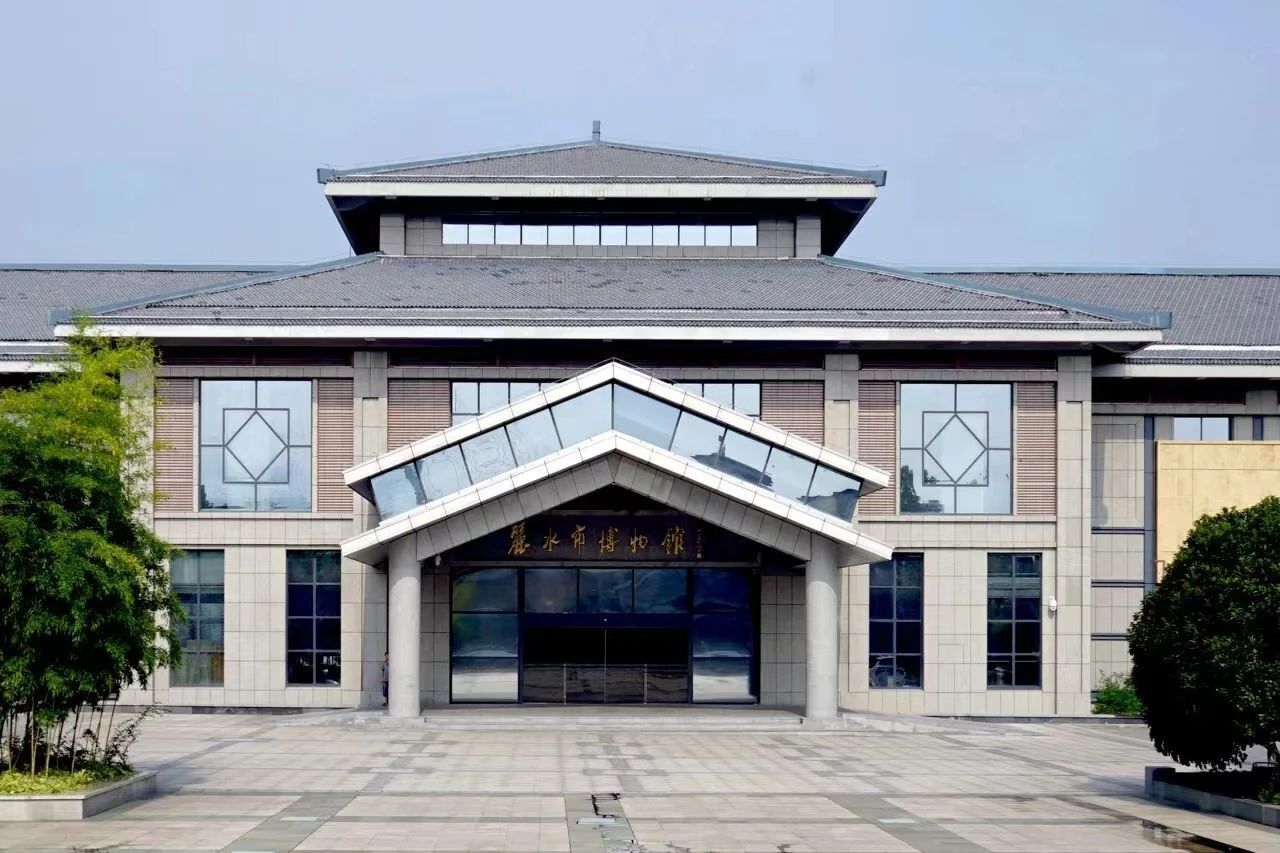 A modern building with a prominent entrance, large windows, and a tiled ground.