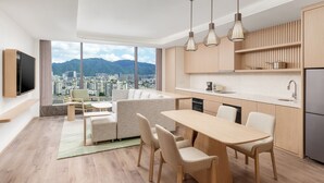 Une cuisine moderne avec des meubles en bois, un coin repas comprenant une table et des chaises, et une grande fenêtre donnant sur la ville.