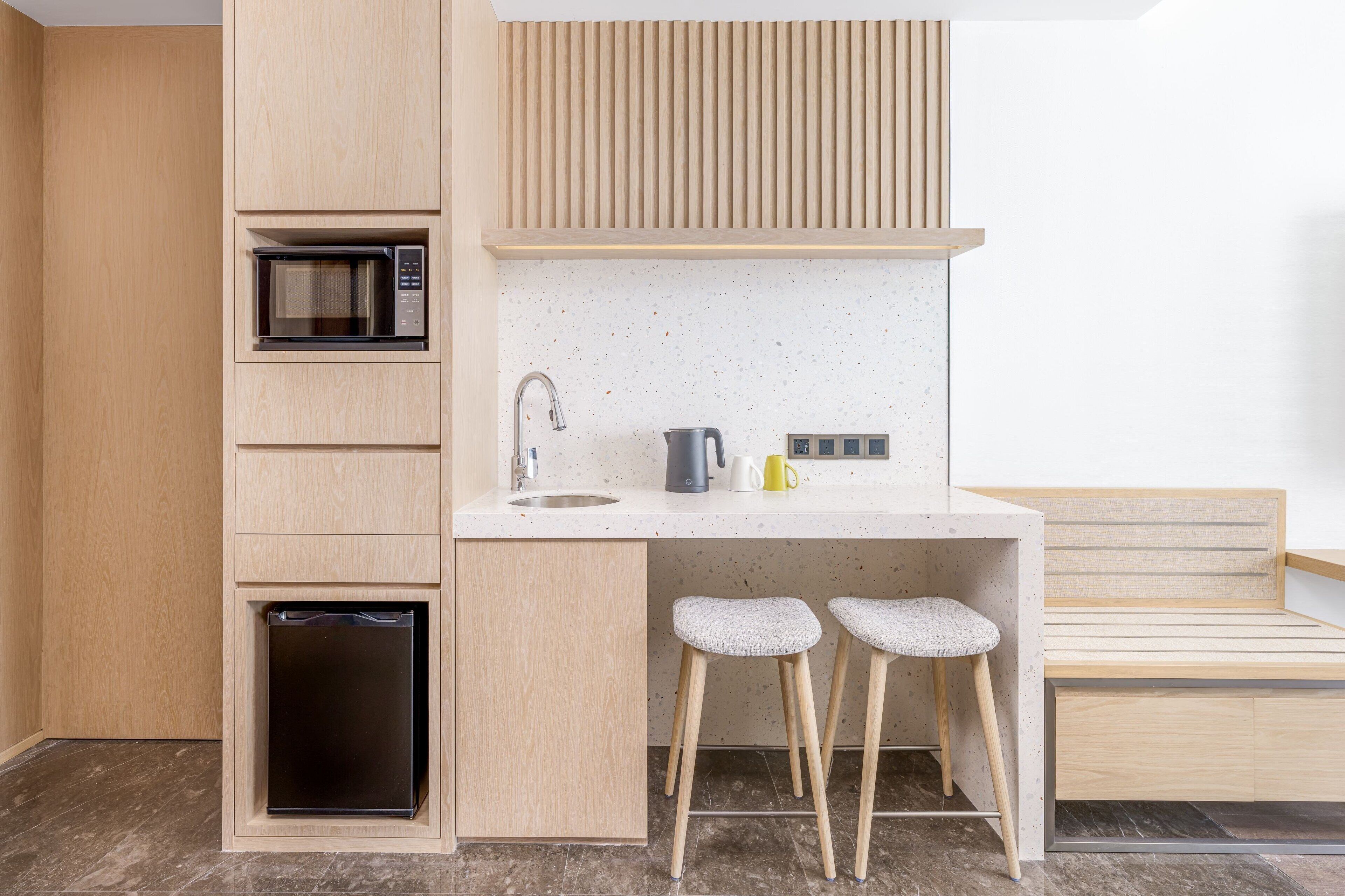 Una cocina compacta con microondas, lavamanos y taburetes de bar.