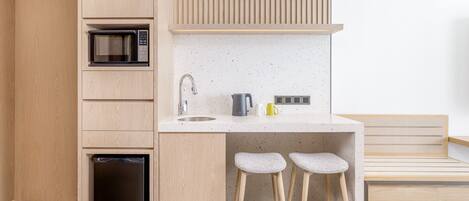 Una cocina compacta con microondas, lavamanos y taburetes de bar.