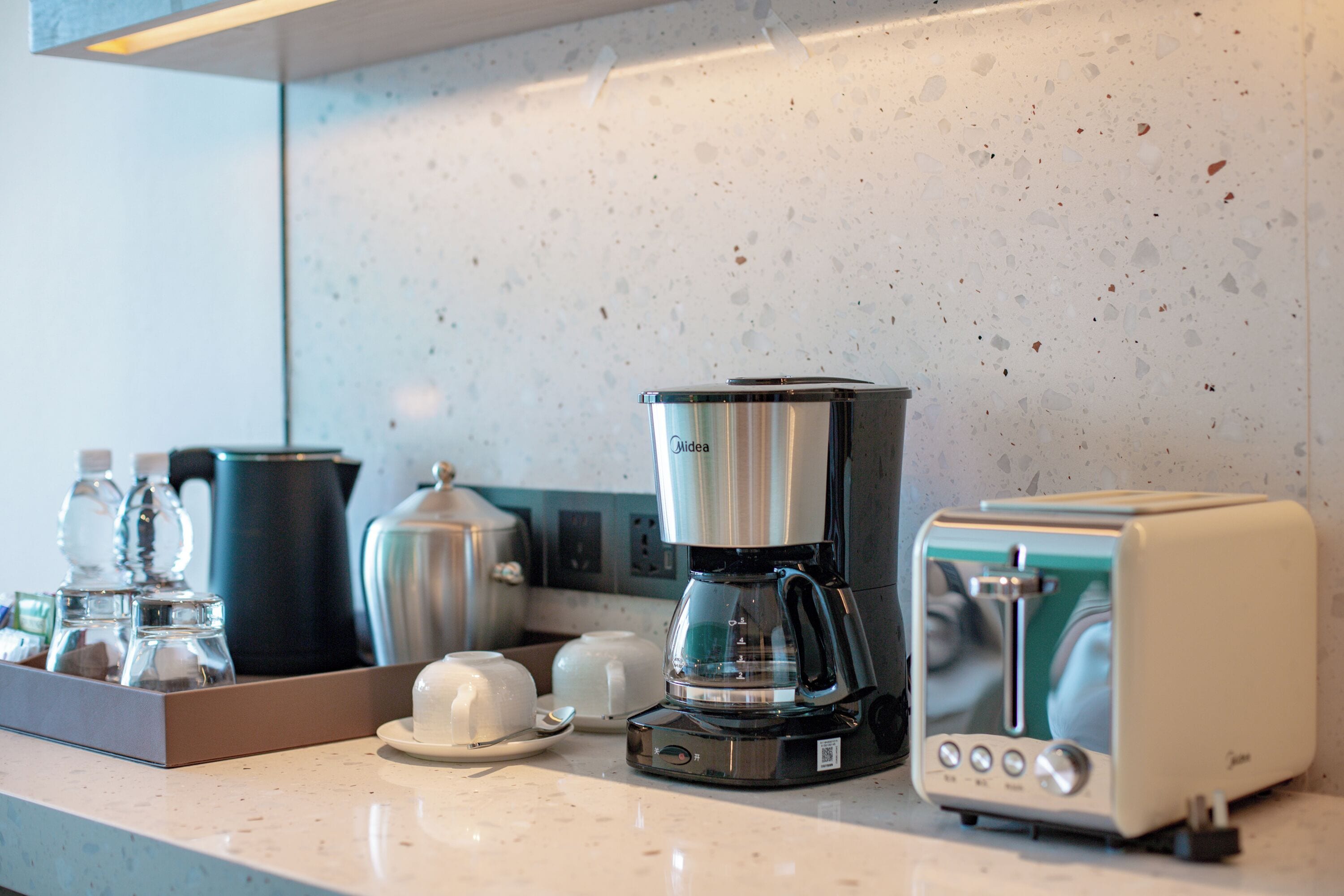 A kitchenette with a coffee maker, toaster, and water bottles on the counter.
