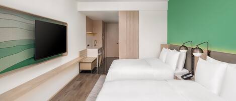 A modern hotel room with a large bed, a television mounted on the wall, a desk with a chair, and a green accent wall.