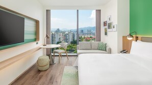 A modern hotel room with a large bed, a small round table, a sofa, and a TV mounted on the wall.