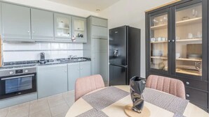 Une cuisine moderne avec des meubles gris, un réfrigérateur noir et un coin repas comprenant deux chaises et une table.