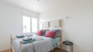 Une chambre à coucher avec un lit, une petite table sur laquelle est posée une plante, et une fenêtre.