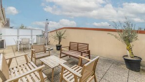 Un espace patio aménagé avec du mobilier en bois, notamment des chaises et des tables, ainsi qu’une plante en pot.