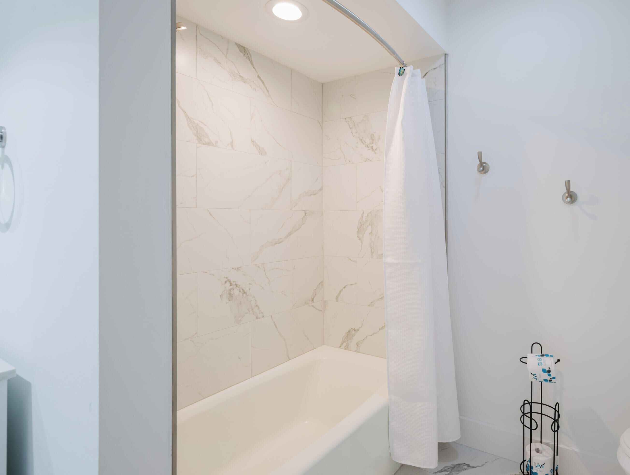 A modern bathroom with a bathtub, a shower curtain, and a toilet paper holder.