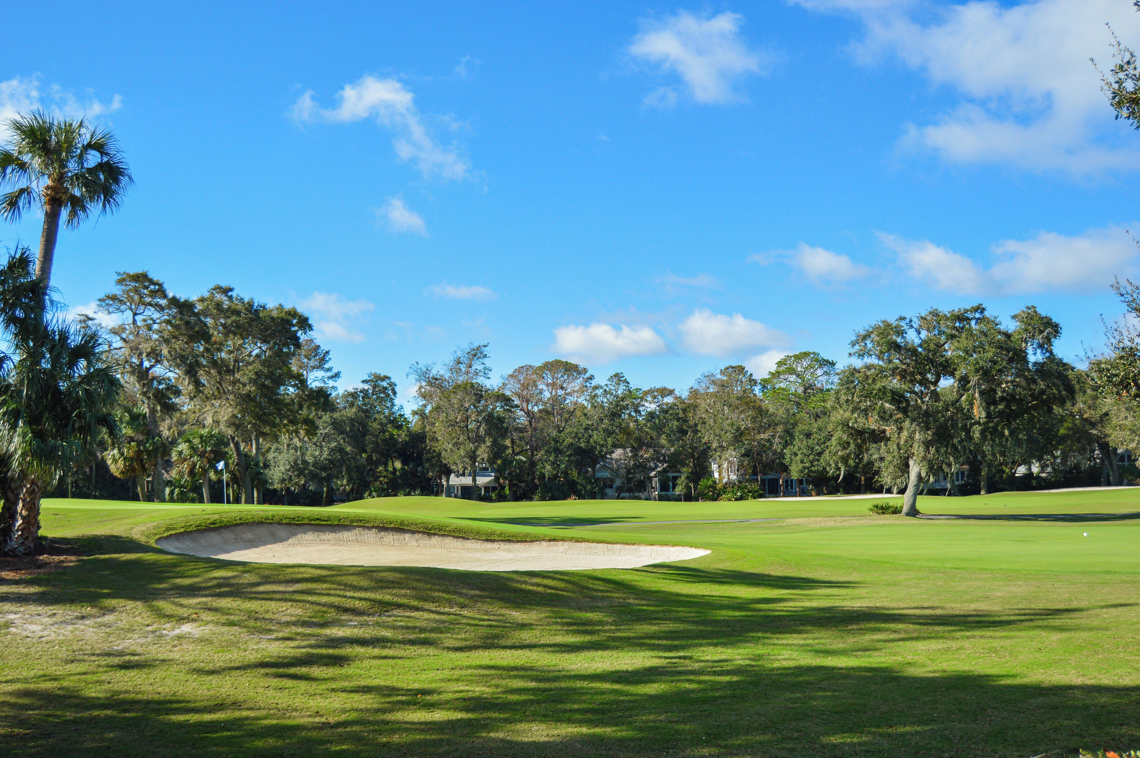 A golf course with a sand bunker, trees, and a clear blue sky.