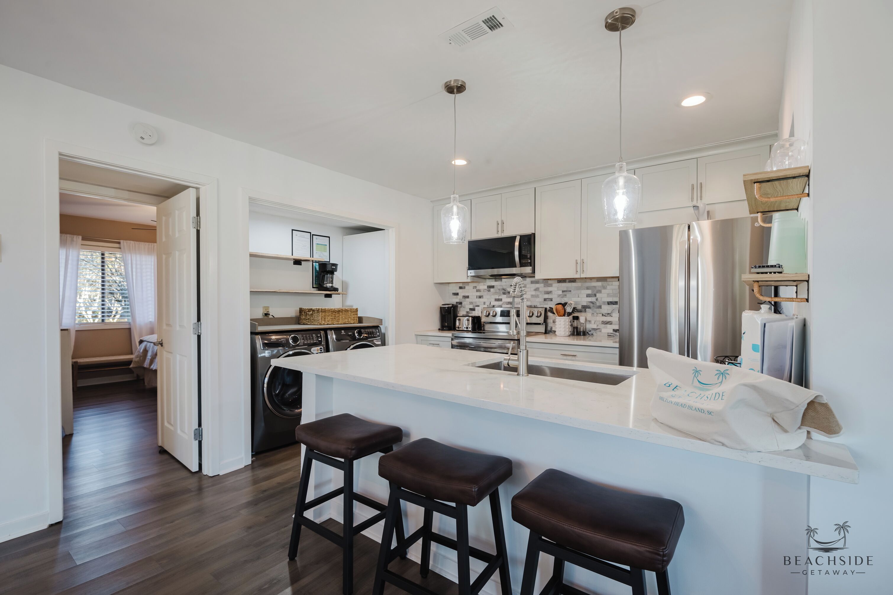 A modern kitchen with a central island, bar stools, stainless steel appliances, and pendant lighting.